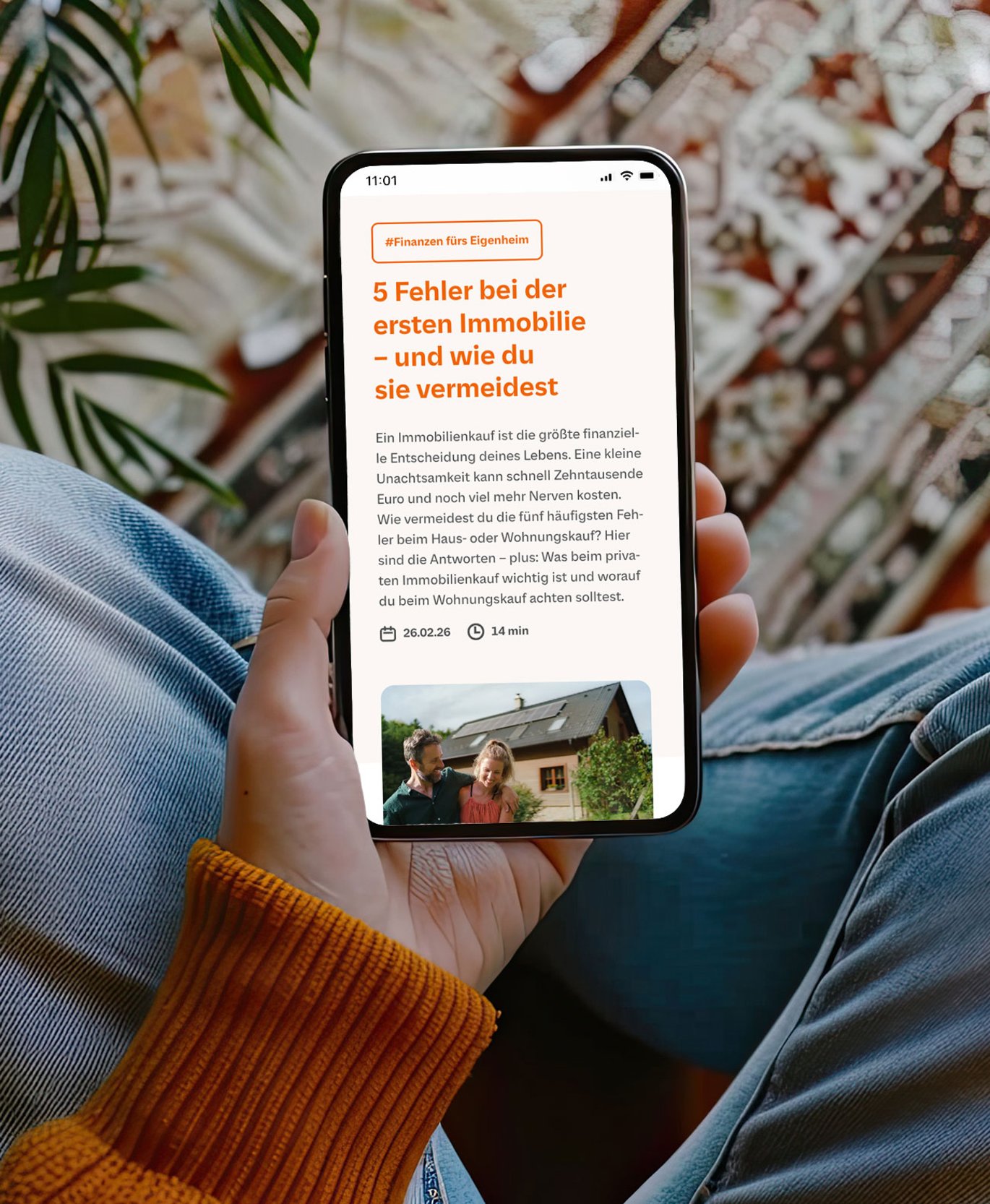 Smartphone in einer Hand zeigt einen Artikel über Immobilienfinanzierung („5 Fehler bei der ersten Immobilie“), im Hintergrund eine gemütliche Wohnsituation mit Pflanzen.